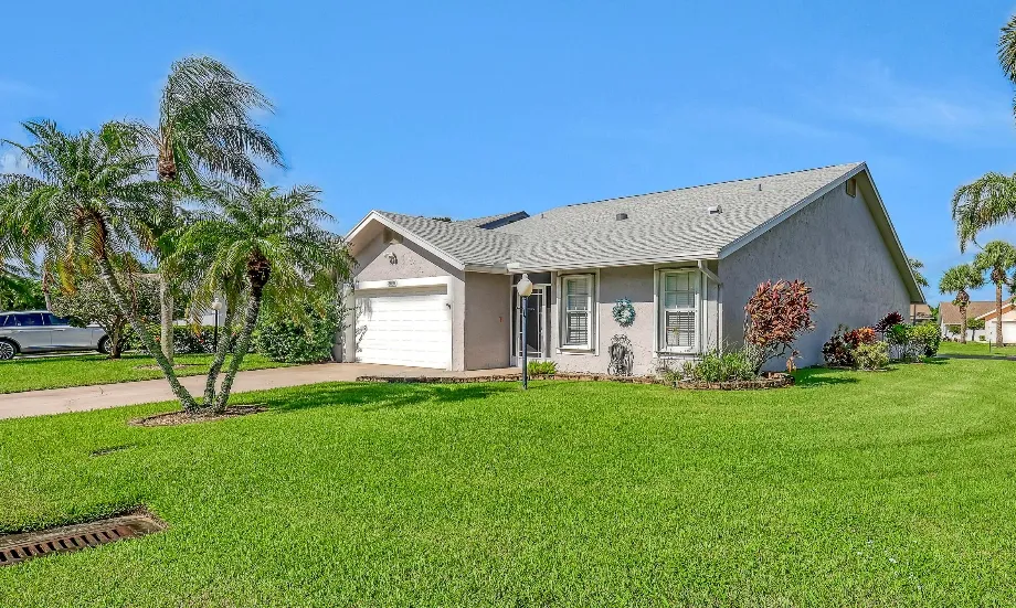 Single-story Palm Beach County home with a green lawn and palm trees